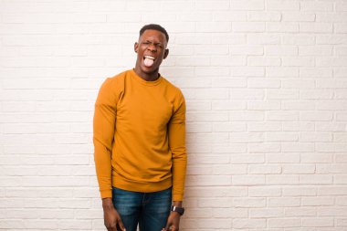 Genç Afro-Amerikan siyah adam neşeli, kaygısız, asi tavırlı, şakacı ve dil çıkartan, tuğla duvara karşı eğlenen