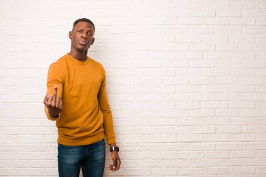 Genç Afro-Amerikan siyahi adam kızgın, sinirli, asi ve agresif hissediyor, orta parmağını şaklatıyor, tuğla duvara karşı savaşıyor.