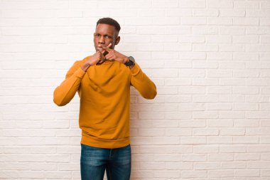 Genç Afro-Amerikan siyahi adam ciddi görünüyor ve reddedilmek için iki parmağını da öne uzatıp tuğla duvara karşı sessizlik istiyor.