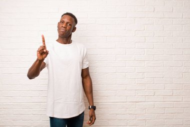 Genç Afro-Amerikan siyahi adam gülümsüyor ve arkadaş canlısı görünüyor, bir numara ya da ilk eli önde, tuğla duvara doğru sayıyor.
