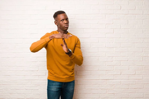 young african american black man looking serious, stern, angry and displeased, making time out sign against brick wall