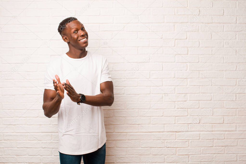 young african american black man feeling happy and successful, smiling and clapping hands, saying congratulations with an applause against brick wall