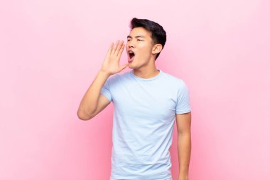 Genç Çinli adam öfkeyle bağırarak kenardaki boşluğu kopyalamasını söylüyor. Düz renkli duvara karşı eli ağzının yanında.