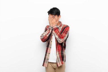 Genç Çinli bir adam korkmuş ya da utanmış hisseder. Gözleri yarı çıplak bir şekilde duvara bakar ya da gözetler.