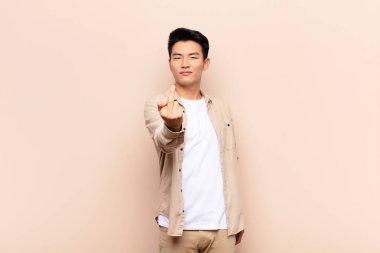 Genç Çinli bir adam kızgın, sinirli, isyankar ve agresif orta parmağını sallayarak düz renkli duvara karşı savaşıyor.