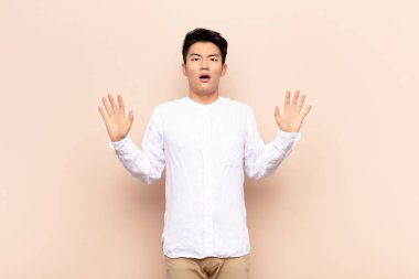 Genç Çinli adam sersemlemiş ve korkmuş hissediyor, korkunç bir şeyden korkuyor, elleri önde ve düz renkli duvardan uzak durun diyor.