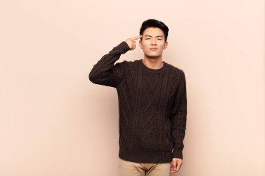 Genç Çinli adam şaşkın ve şaşkın hissediyor. Deli, deli ya da düz renkli duvara karşı aklını kaçırmış olduğunu gösteriyor.