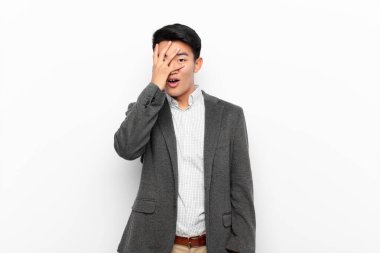 Genç Çinli adam şok olmuş, korkmuş ya da korkmuş görünüyordu. Yüzü elle kaplıydı ve parmaklarının arasından düz duvara bakıyordu.