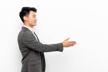 Genç Çinli adam gülümsüyor, sizi selamlıyor ve başarılı bir anlaşma için el sıkışmayı teklif ediyor.