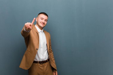 Genç yakışıklı adam gülümsüyor ve arkadaş canlısı görünüyor, bir numara ya da ilk eli önde, düz arkaplanda geriye doğru sayıyor.