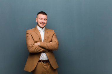 Genç, yakışıklı bir iş adamı gibi görünüyor. Mutlu, gururlu ve tatmin olmuş görünüyor. Kolları düz arkaplanda birleşmiş başarılı bir şekilde gülümsüyor.