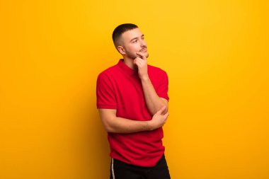 Genç yakışıklı adam mutlu bir şekilde gülümsüyor ve hayal kuruyor ya da şüphe ediyor, düz arkaplana bakıyor.