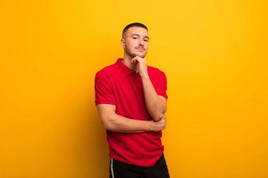 Genç yakışıklı adam mutlu görünüyor ve gülümsüyor, merak ediyor ya da soru soruyor, düz arkaplan ile seçenekleri karşılaştırıyor.