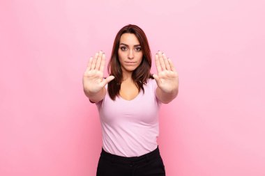 Genç ve güzel bir kadın ciddi, mutsuz, kızgın ve hoşnutsuz görünüyor. Ya da her iki avucunuzu pembe duvara dayayıp durun diyor.