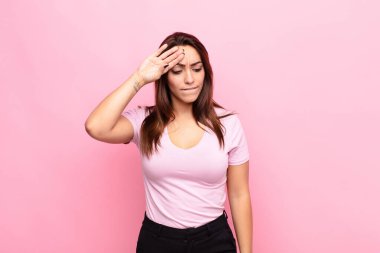 Genç, güzel bir kadın stresli, yorgun ve hayal kırıklığına uğramış görünüyor. Alnından ter akıyor. Pembe duvara karşı umutsuz ve bitkin hissediyor.