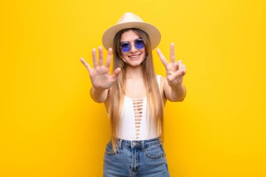 Genç ve güzel bir bayan gülümsüyor ve dost canlısı görünüyor, 7 ya da 7 numarayı gösteriyor, eli önde, geriye doğru sayıyor.