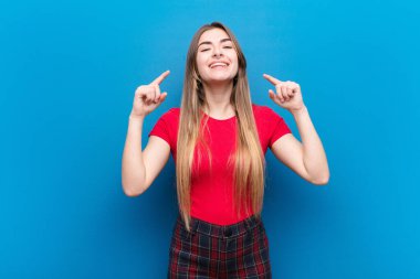 Genç, güzel bir kadın iki eliyle kendi gülümsemesini çiziyor, olumlu ve mutlu görünüyor, mavi duvara karşı sağIık kavramı.