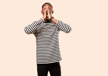 Genç Afro-Amerikan siyahi adam mutlu, heyecanlı ve pozitif hissediyor, elleri ağızın yanında bağırıyor, bej rengi duvara karşı bağırıyor.