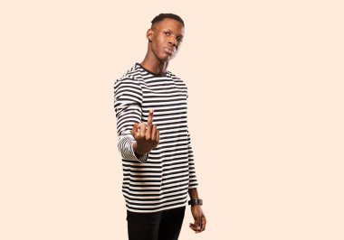 Genç Afro-Amerikan siyahi adam kızgın, sinirli, asi ve agresif hissediyor, orta parmağını sallıyor, bej rengi duvara karşı savaşıyor.