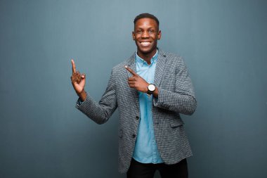 Genç Afro-Amerikan siyahi adam mutlu bir şekilde gülümsüyor ve her iki eli de fotokopi odasında grunge duvarına karşı objeler gösteriyor.