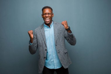 Genç Afrikalı Amerikalı siyahi adam son derece mutlu ve şaşırmış görünüyor, başarıyı kutluyor, bağırıyor ve grunge duvarına karşı zıplıyor.