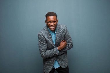 Genç Afro-Amerikan siyahi adam endişeli, hasta, hasta ve mutsuz hissediyor. Ağrılı bir mide ağrısı ya da grunge duvarına karşı grip.