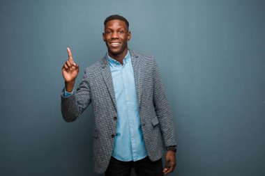 Genç Afro-Amerikan siyahi adam neşeyle ve mutlu bir şekilde gülümsüyor, bir eliyle grunge duvarına uzayı kopyalıyor.