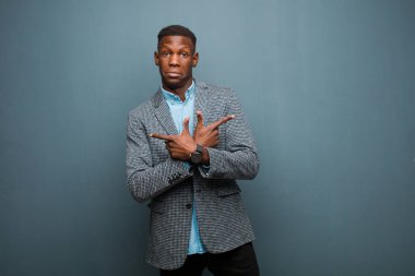 Genç Afro-Amerikan siyahi adam şaşkın ve şaşkın görünüyor, güvensiz ve zıt yönleri işaret ediyor grunge duvarına karşı şüpheyle