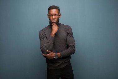 Genç Afro-Amerikan siyahi adam ciddi, kafası karışmış, kararsız ve düşünceli görünüyor. Grunge Wall karşısında seçenekler ve tercihler arasında şüpheci görünüyor.