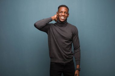 Genç Afro-Amerikan siyahi adam neşeli ve kendinden emin bir şekilde gülümsüyor, mutlu, dostça bir gülümsemeyle grunge duvarına karşı.