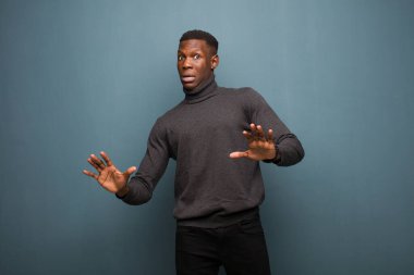 Genç Afrikalı Amerikalı siyahi adam sersemlemiş ve korkmuş hissediyor, korkunç bir şeyden korkuyor, elleri açık ve grunge duvarından uzak durun diyor.