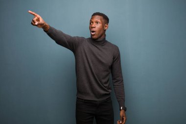 Genç Afro-Amerikan siyahi adam şokta ve şaşırmış hissediyor, şaşkınlıkla bakıyor ve hayranlıkla bakıyor grunge duvarına karşı.