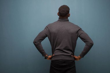 Genç Afro-Amerikan siyahi adam kafası karışık ya da dolu hissediyor ya da şüphe ve sorular, merak ediyor, elleri kalçasında, dikiz aynasıyla grunge duvarına bakıyor