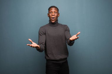 Genç Afro-Amerikan siyahi adam aşırı derecede şaşırmış, şaşırmış, endişeli ve paniklemiş hissediyor. Stresli ve dehşete düşmüş bir şekilde grunge duvarına bakıyor.