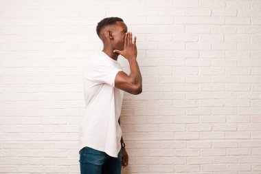 Genç Afro-Amerikan siyahi adam profili, mutlu ve heyecanlı görünüyor, bağırıyor ve duvarın kenarına uzayı kopyalamak için çağırıyor.