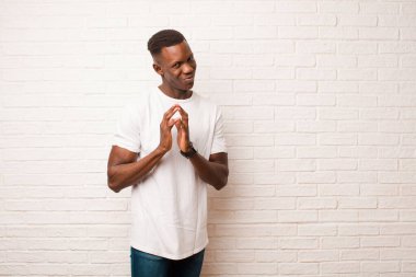 Genç Afrikalı Amerikalı siyahi adam gururlu, yaramaz ve kibirli hissederken şeytani bir plan kuruyor ya da tuğla duvara karşı bir numara düşünüyor.