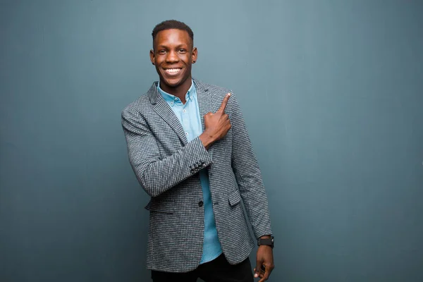 young african american black man smiling cheerfully, feeling happy and pointing to the side and upwards, showing object in copy space