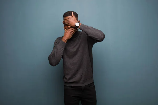 young african american black man covering face with both hands saying no to the camera! refusing pictures or forbidding photos against grunge wall