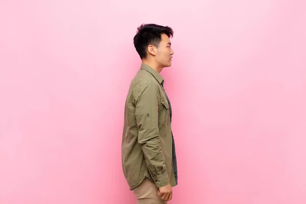 young chinese man on profile view looking to copy space ahead, thinking, imagining or daydreaming against flat color wall