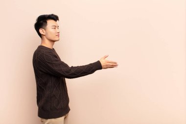 Genç Çinli adam gülümsüyor, sizi selamlıyor ve başarılı bir anlaşma için el sıkışmayı teklif ediyor.