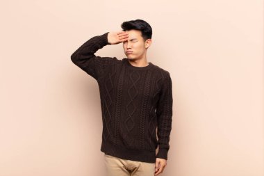 Genç Çinli adam stresli, yorgun ve hayal kırıklığına uğramış görünüyor, alnından ter damlıyor, umutsuz ve bitkin hissediyor.