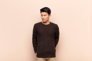 Genç Çinli bir adam üzgün, üzgün ya da kızgın ve olumsuz bir tavır takınıyor, düz renk duvarına karşı anlaşmazlık içinde.