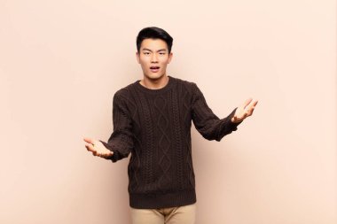 Genç Çinli adam kendini mutlu, şaşkın, şanslı ve şaşırmış hissediyor. Sanki her şeyi ciddiye alıyormuş gibi. Düz renkli duvara karşı inanılmaz.