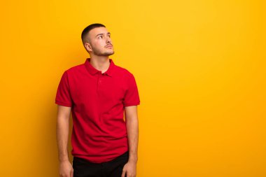 Endişeli, kafası karışık, budala bir ifadeyle genç yakışıklı bir adam kopya alanı arıyor, düz arkaplana karşı şüpheyle bakıyor.