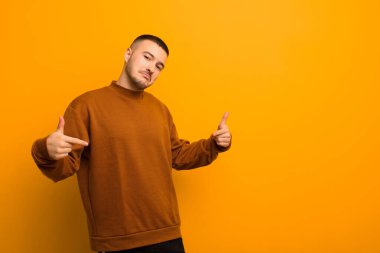 Genç yakışıklı adam gururlu, kibirli, mutlu, şaşırmış ve tatmin olmuş görünüyor, kendini göstererek, düz arkaplan karşısında bir kazanan gibi hissediyor.