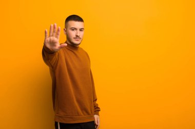 Genç yakışıklı adam ciddi, sert, hoşnutsuz ve kızgın görünüyor. Avuç içini açıp düz arkaplana karşı jestleri durduruyor.