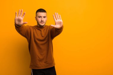 Genç yakışıklı adam ciddi, mutsuz, sinirli ve hoşnutsuz görünüyor. Ya da her iki avuç içi de düz arkaplan karşısında durarak dur diyor.