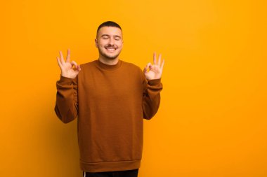 Genç yakışıklı adam konsantre olmuş ve meditasyon yapıyor, kendini tatmin olmuş ve rahat hissediyor, düşünüyor ya da düz arkaplan karşısında bir seçim yapıyor.