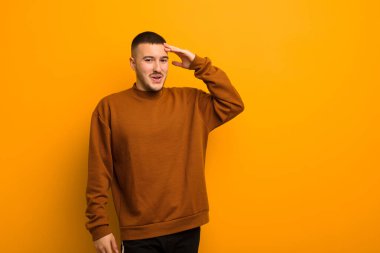 Genç yakışıklı adam mutlu, şaşkın ve şaşırmış görünüyor, gülümsüyor ve düz arkaplan karşısında inanılmaz ve inanılmaz iyi haberler veriyor.