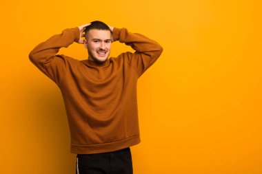 Genç, yakışıklı bir adam stresli, endişeli, endişeli ya da korkmuş, elleri başının üstünde, düz arkaplanda panikliyor.